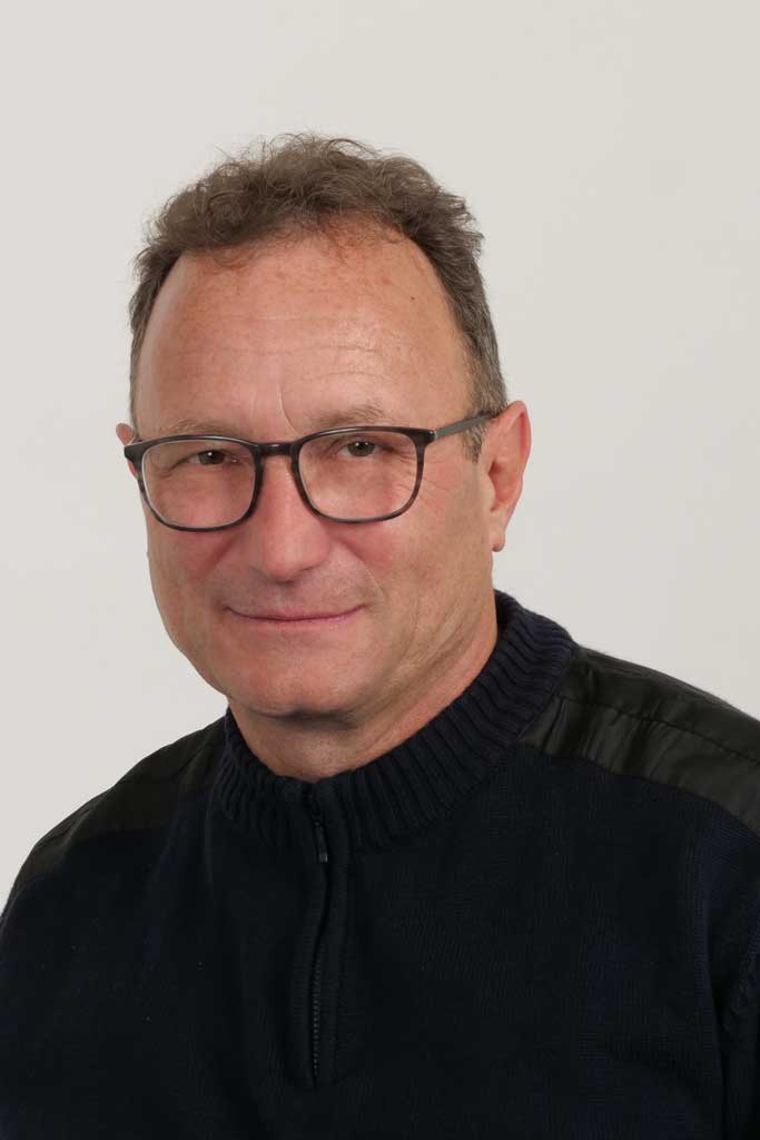 Ein Mann mittleren Alters mit Brille und kurzen Haaren, der einen dunklen Pullover trägt, lächelt leicht. Ein Mann mittleren Alters mit Brille und kurzen Haaren, der einen dunklen Pullover trägt, lächelt leicht.