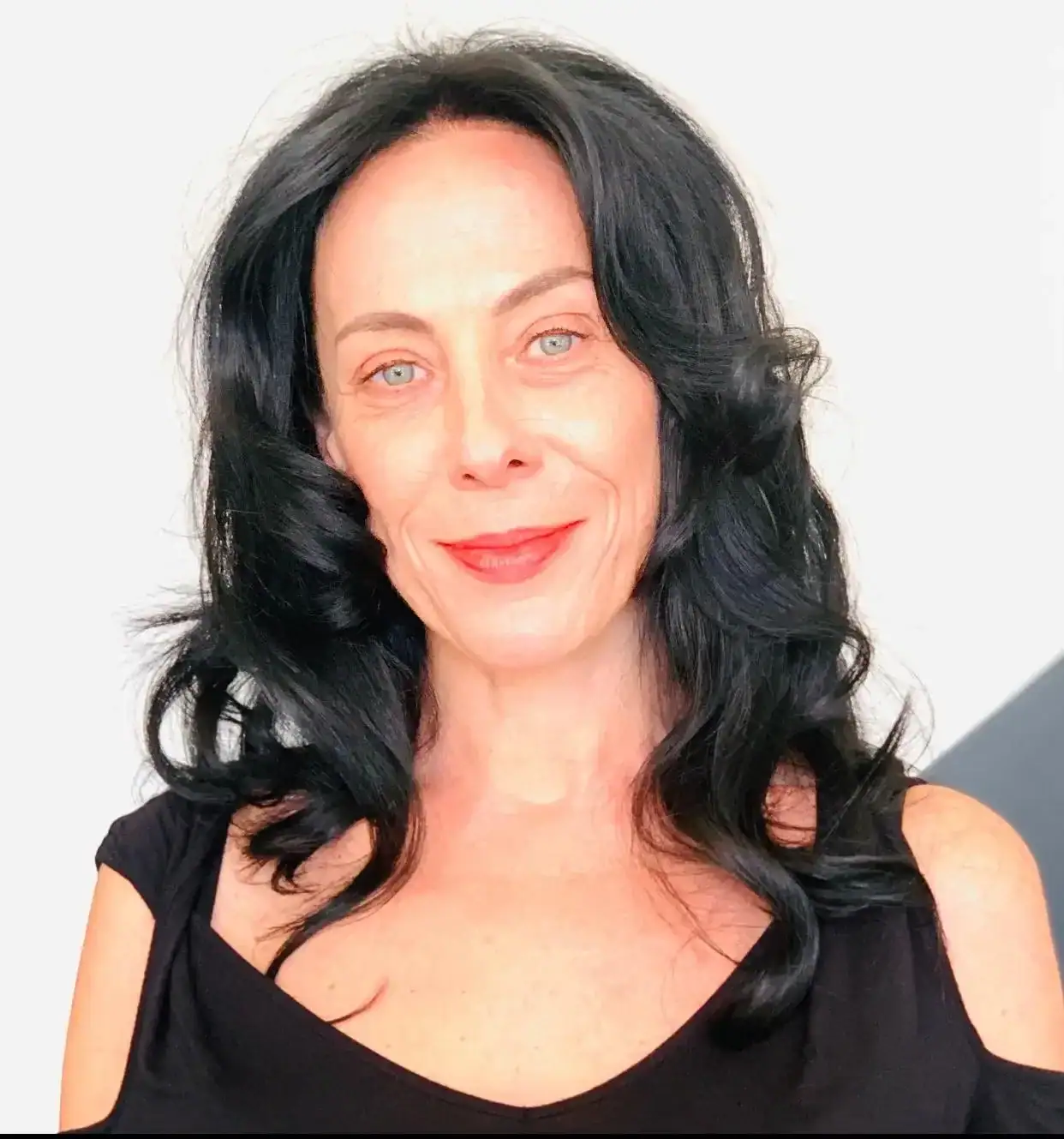 WhatsApp-Image-2025-10-16-at-19.40.36 Frau mit langen dunklen Haaren in einem roten Oberteil, lächelnd vor einem schlichten hellen Hintergrund.