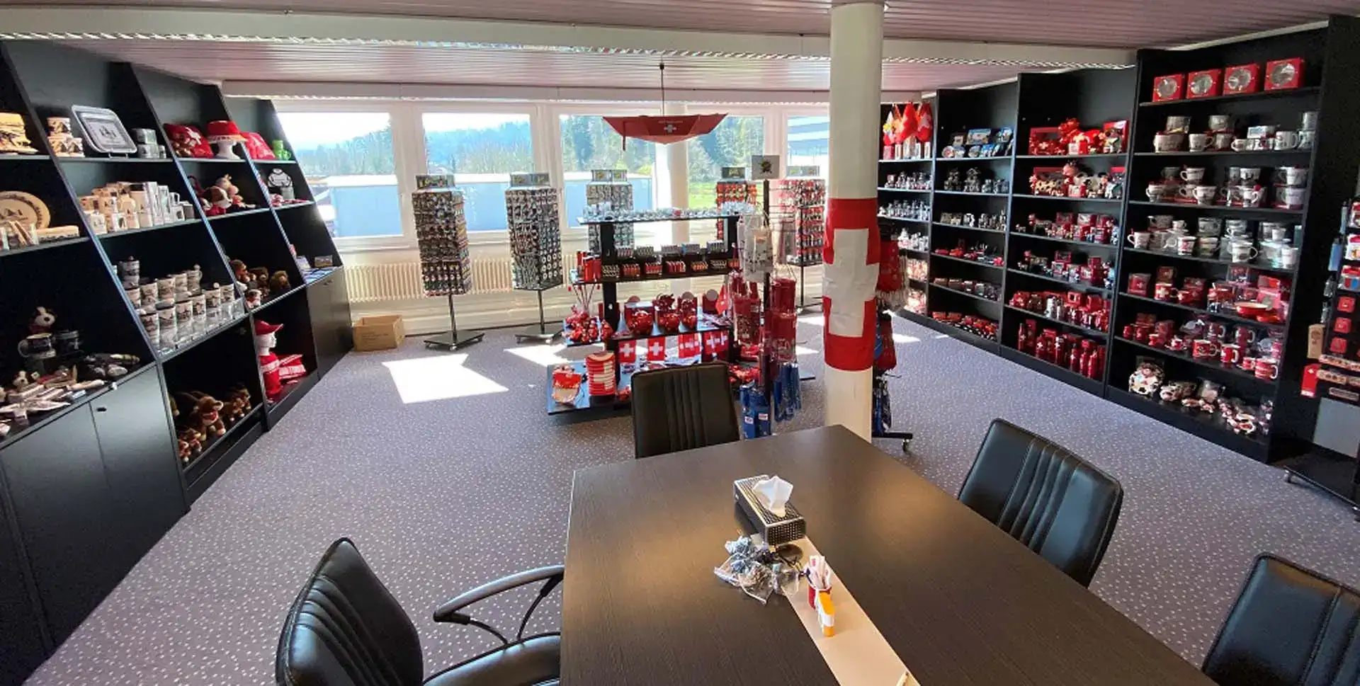 Raum mit Regalen mit roten und schwarzen Souvenirs, Ausstellungsregalen und einem Besprechungstisch mit Stühlen. Raum mit Regalen mit roten und schwarzen Souvenirs, Ausstellungsregalen und einem Besprechungstisch mit Stühlen.