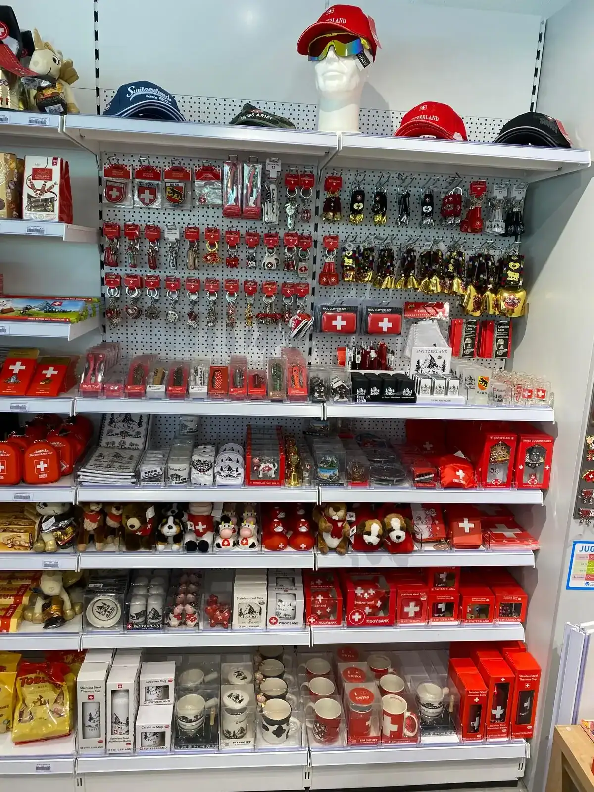 Regale gefüllt mit Schweizer Souvenirs von grosshandel schweiz, darunter Tassen, Hüte und Schlüsselanhänger. Regale gefüllt mit Schweizer Souvenirs von grosshandel schweiz, darunter Tassen, Hüte und Schlüsselanhänger.